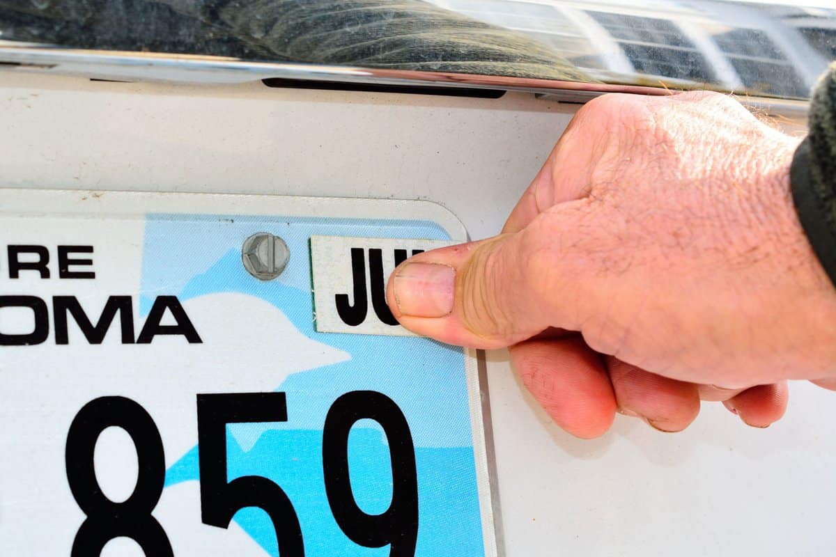 a male thumb pressing the required month tag for an annual license registration on rear license plate